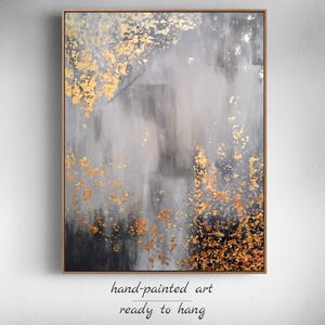 May include: Abstract painting with gray and gold tones. The painting has a textured surface and is framed in a wooden frame. The text "hand-painted art ready to hang" is written below the painting.