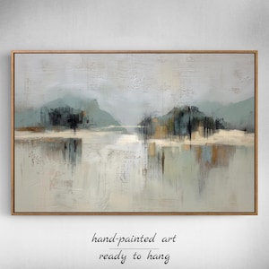 May include: Abstract landscape painting in a wooden frame. The artwork features muted tones of gray, blue, and brown, depicting a serene scene with mountains and water. The text at the bottom reads "hand-painted art ready to hang."