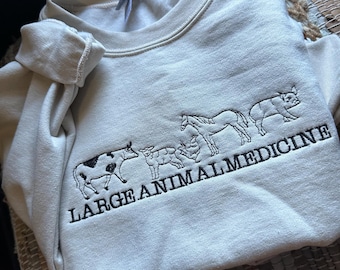 May include: A cream-colored sweatshirt with a black embroidered design of a cow, sheep, horse, and pig with the text "LARGE ANIMAL MEDICINE".