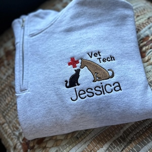 Puede incluir: Sudadera gris con una cruz roja, un perro y un gato, y el texto "Vet Tech Jessica" bordado en la parte delantera.