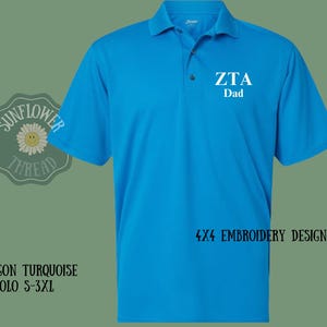Può includere: Una polo blu turchese con il testo "ZTA Dad" ricamato sul davanti. La polo è un design di ricamo 4x4.