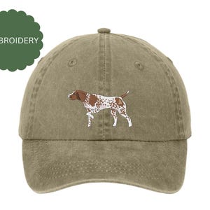 Puede incluir: Una gorra de béisbol verde caqui con una imagen bordada de un perro Braco Alemán de Pelo Corto marrón y blanco.