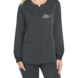 May include: A charcoal gray zip-up scrub jacket with a black ribbed cuff. The jacket has two front pockets and a small embroidered heart with a heartbeat line and the text "Alexis RN, BSN".