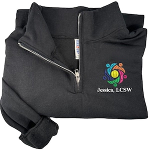 May include: Black quarter-zip sweatshirt with a silver zipper and a colorful embroidered design. The text "Jessica, LCSW" is embroidered below the design. The sweatshirt is made by Jerzees.