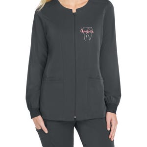 May include: A charcoal gray zip-up scrub jacket with a white tooth graphic and the name "Amber" embroidered in pink on the left chest.