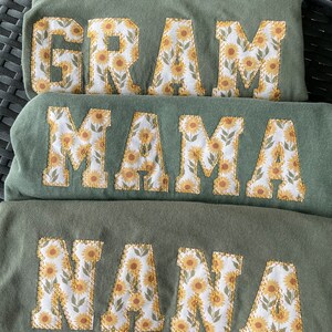 May include: Three green shirts with the words "GRAM", "MAMA", and "NANA" embroidered in white with a sunflower pattern.