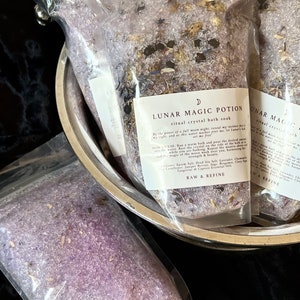 May include: A close-up of two clear plastic bags filled with purple bath salts. The bags are labeled "Lunar Magic Potion Ritual Crystal Bath Soak" and include a list of ingredients. The text reads "By the power of a full moon night, reveal my inner strength and beauty. How to Use: Run a warm bath and pour the desired amount of bath salts into the water while you are bathing. Repeat the mantra as you feel it. Ingredients: Epsom Salt, Dead Sea Salt, Lavender, Chamomile, Calendula, Rose, Lavender, Bergamot, Clary Sage, Tangerine & Cypress Essential Oils. Raw & Refine."