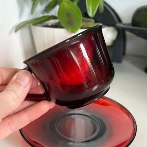 May include: A red glass teacup and saucer set. The cup and saucer are both a deep red color and have a glossy finish.