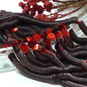 May include: A strand of red and brown sequins, with the red sequins stacked on top of the brown sequins. The sequins are arranged in a loose coil.