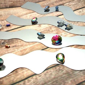 May include: Five wavy, silver-colored metal strips with iridescent gemstones of various shapes and sizes placed on top. The gemstones are a mix of round, teardrop, and oval shapes.