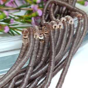 May include: A strand of brown metallic sequins, strung together to form a long chain. The sequins are flat and round, with a slightly raised center. The chain is lying on a white surface.