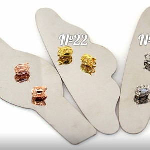 May include: Three pairs of earrings displayed on a silver background. The earrings are in three different colors: rose gold, gold, and silver. The earrings are all the same style, with a small, round design.