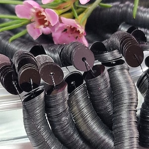 May include: A close-up of a pile of black sequins, each one stacked on top of the other. The sequins are arranged in a circular pattern, creating a spiral effect. The sequins are shiny and reflect light.