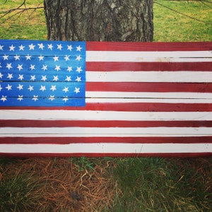 May include: A wooden American flag painted in red, white, and blue. The flag is made of reclaimed wood planks and has a rustic look.