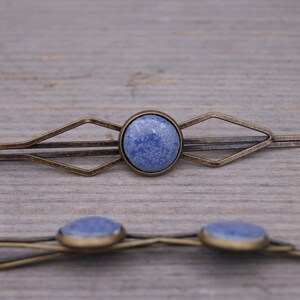 Puede incluir: Dos pinzas para el pelo de bronce antiguo con detalles de piedra azul. La pinza m&aacute;s grande tiene un dise&ntilde;o geom&eacute;trico y la m&aacute;s peque&ntilde;a es una barra simple.