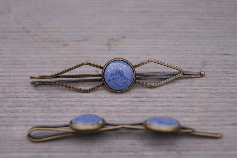 Puede incluir: Dos pinzas para el pelo de bronce antiguo con detalles de piedra azul. La pinza m&aacute;s grande tiene un dise&ntilde;o geom&eacute;trico y la m&aacute;s peque&ntilde;a es una barra simple.