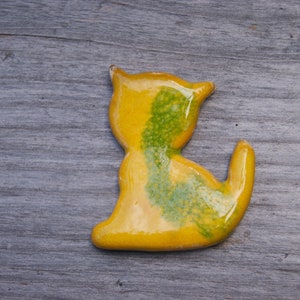 May include: A yellow ceramic cat figurine with green accents. The cat is sitting with its tail curled around its body.