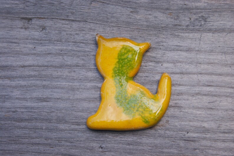 May include: A yellow ceramic cat figurine with green accents. The cat is sitting with its tail curled around its body.