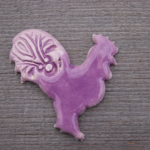 May include: A purple ceramic rooster figurine with a detailed design on its tail feathers.