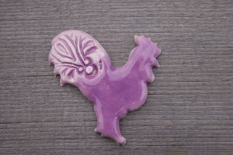 May include: A purple ceramic rooster figurine with a detailed design on its tail feathers.