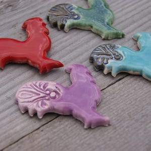 May include: Four ceramic rooster figurines in different colors: red, green, blue, and purple. Each rooster has a unique design and is a decorative piece.