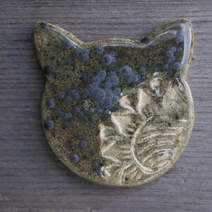 Puede incluir: Una figurita de cer&aacute;mica de un gato con un esmalte verde y marr&oacute;n. El gato tiene un dise&ntilde;o detallado con manchas negras y un patr&oacute;n floral.