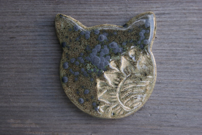 Puede incluir: Una figurita de cer&aacute;mica de un gato con un esmalte verde y marr&oacute;n. El gato tiene un dise&ntilde;o detallado con manchas negras y un patr&oacute;n floral.