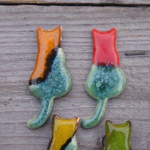 May include: Four ceramic cat figurines in various colors, including orange, red, yellow, and green. The cats are all facing forward with their tails curled behind them.