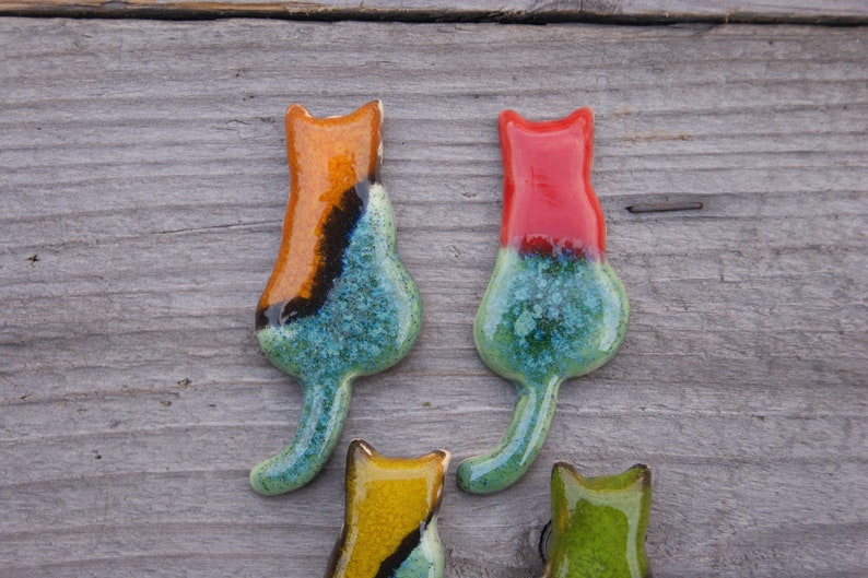 May include: Four ceramic cat figurines in various colors, including orange, red, yellow, and green. The cats are all facing forward with their tails curled behind them.