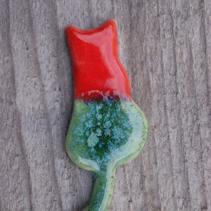 May include: A ceramic cat figurine with a red and green glaze. The cat is sitting with its tail curled around its body.