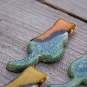 May include: Three ceramic cat figurines in different colors. The first cat is blue, green, and orange. The second cat is yellow, green, and black. The third cat is red, green, and blue.