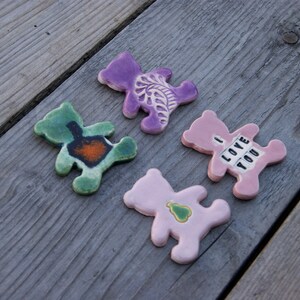 May include: Four ceramic bear figurines with different designs. One is purple with a floral design, one is green with a brown design, one is pink with a green heart, and one is pink with the text "I LOVE YOU".