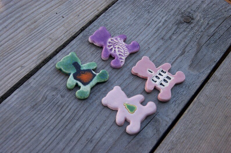 May include: Four ceramic bear figurines with different designs. One is purple with a floral design, one is green with a brown design, one is pink with a green heart, and one is pink with the text "I LOVE YOU".