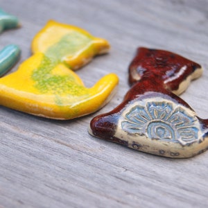May include: Four ceramic cat figurines in different colors. The cats are in a sitting position with their tails curled around their bodies. The cats are painted in shades of blue, yellow, green, and brown.