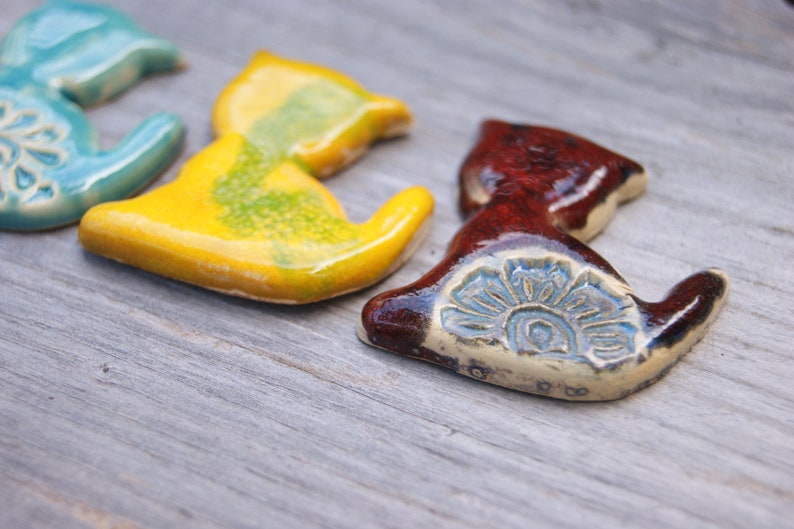 May include: Four ceramic cat figurines in different colors. The cats are in a sitting position with their tails curled around their bodies. The cats are painted in shades of blue, yellow, green, and brown.
