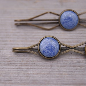 Puede incluir: Dos pinzas para el pelo de oro antiguo con adornos de cer&aacute;mica azul. La cer&aacute;mica tiene un patr&oacute;n moteado.