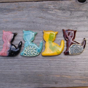 May include: Five ceramic cat figurines in different colors, including pink, black, blue, yellow, and brown. Each figurine has a unique design and is painted with intricate details.