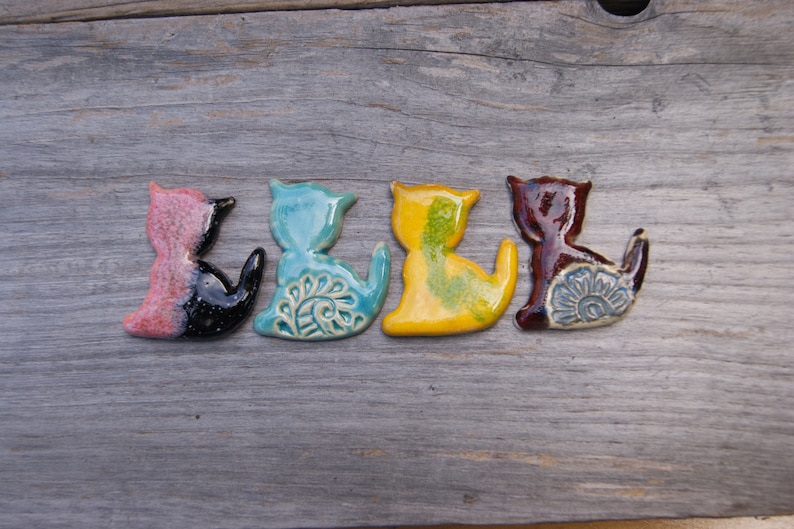 May include: Five ceramic cat figurines in different colors, including pink, black, blue, yellow, and brown. Each figurine has a unique design and is painted with intricate details.