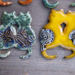 May include: Two ceramic cat figurines, one green and blue with floral designs, the other yellow with white floral designs.