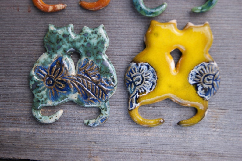 May include: Two ceramic cat figurines, one green and blue with floral designs, the other yellow with white floral designs.