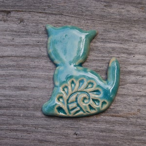 May include: A teal blue ceramic cat figurine with a white swirl design on its back.