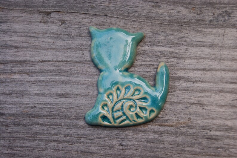 May include: A teal blue ceramic cat figurine with a white swirl design on its back.