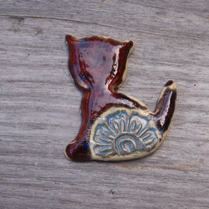 May include: A ceramic cat figurine with a brown glaze and a blue and white floral design on its back.