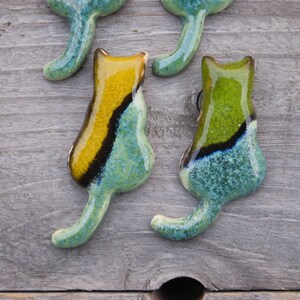 May include: Four ceramic cat figurines with a teal, green, and yellow glaze. The cats are facing different directions and have a textured surface.