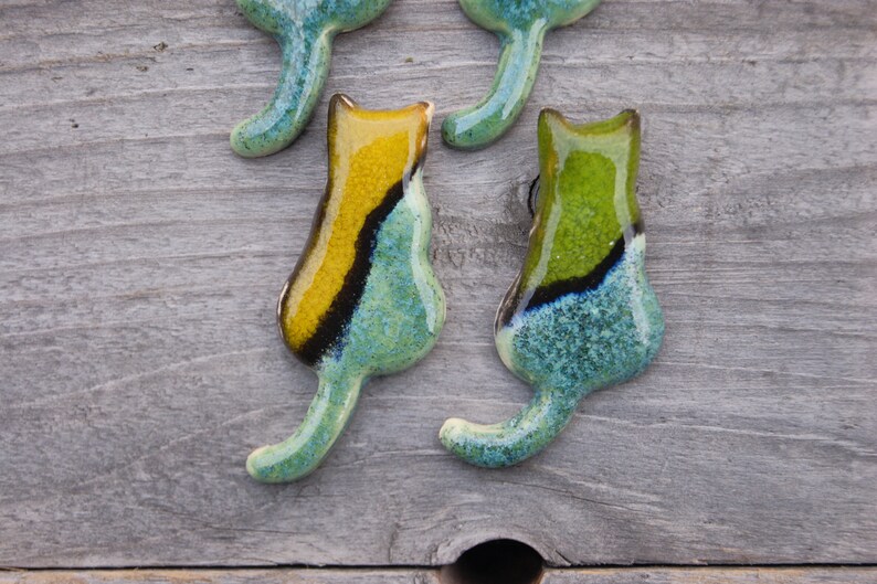May include: Four ceramic cat figurines with a teal, green, and yellow glaze. The cats are facing different directions and have a textured surface.