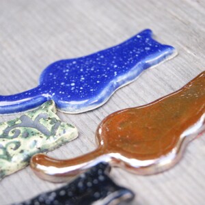 May include: Four ceramic cat figurines in different colors and patterns. The cats are all in a similar pose, with their tails curled around their bodies. The cats are made of a smooth, glossy ceramic.