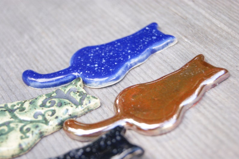 May include: Four ceramic cat figurines in different colors and patterns. The cats are all in a similar pose, with their tails curled around their bodies. The cats are made of a smooth, glossy ceramic.