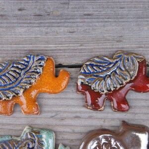 May include: Five ceramic elephant figurines with blue and gold leaf designs. The elephants are in various colors, including orange, red, pink, and brown.