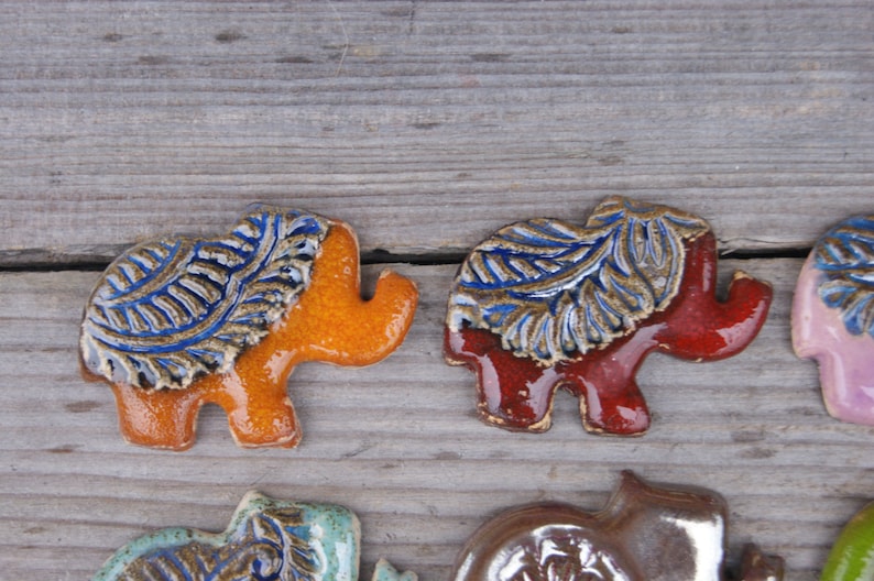 May include: Five ceramic elephant figurines with blue and gold leaf designs. The elephants are in various colors, including orange, red, pink, and brown.