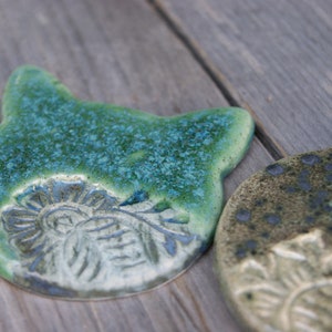Puede incluir: Dos posavasos de cer&aacute;mica con un esmalte verde y azul. Los posavasos presentan un dise&ntilde;o en relieve de una flor.
